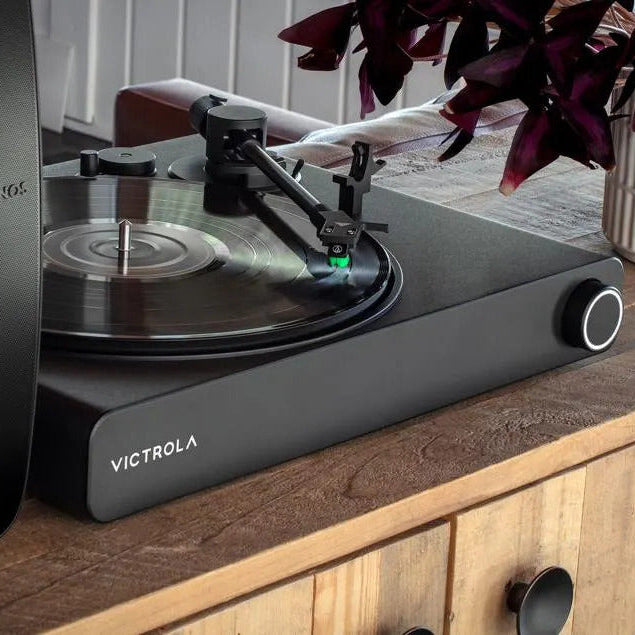 Victrola STREAM ONYX TURNTABLE on a wooden surface with a plant in the background