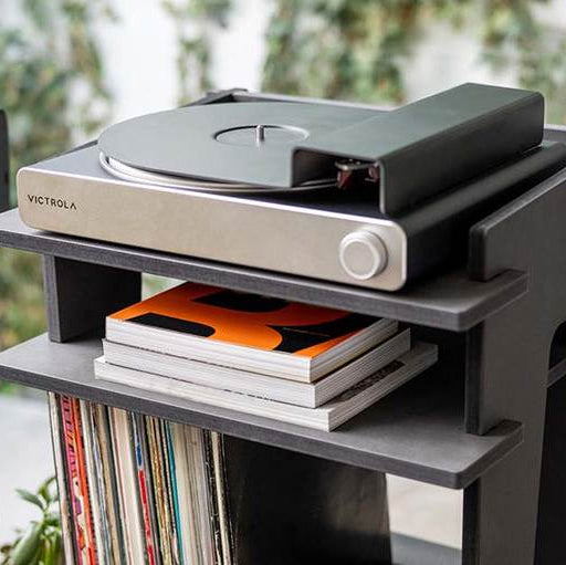 Victrola STREAM CARBON TURNTABLE  on a stand with vinyl records and magazines.